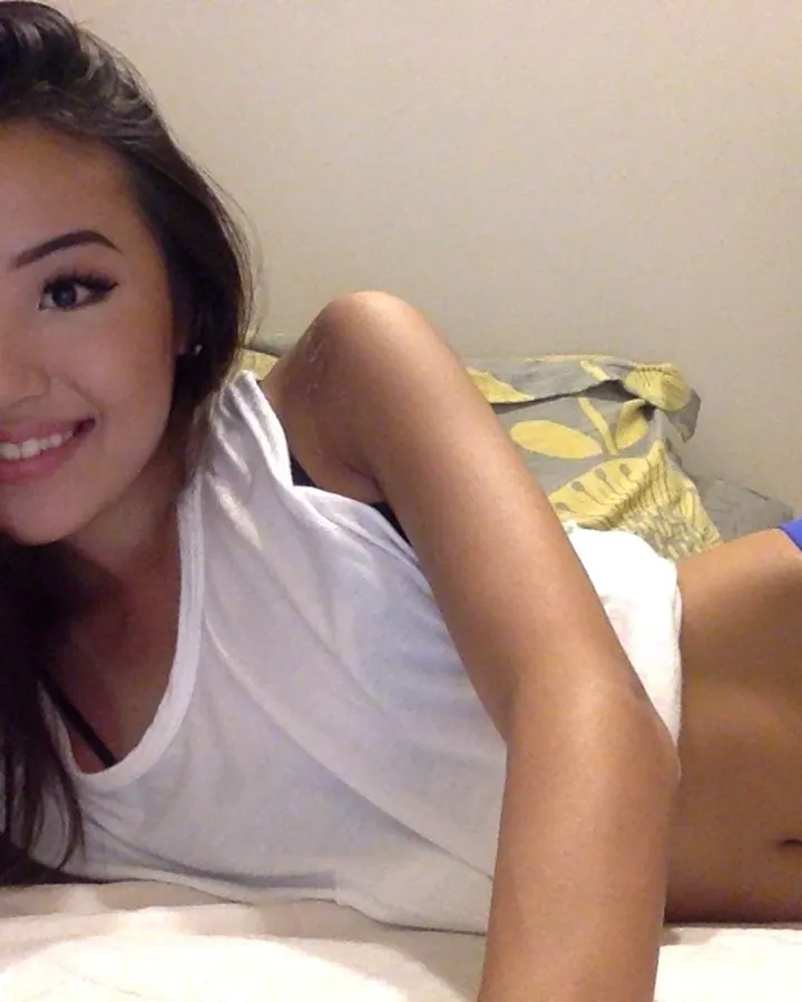 Femme trans asiatique souriante, en haut blanc et sous-vêtements bleus, allongée sur un lit