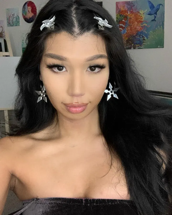 Femme trans asiatique aux cheveux noirs, maquillage soigné, portant des barrettes argentées, regardant la caméra.