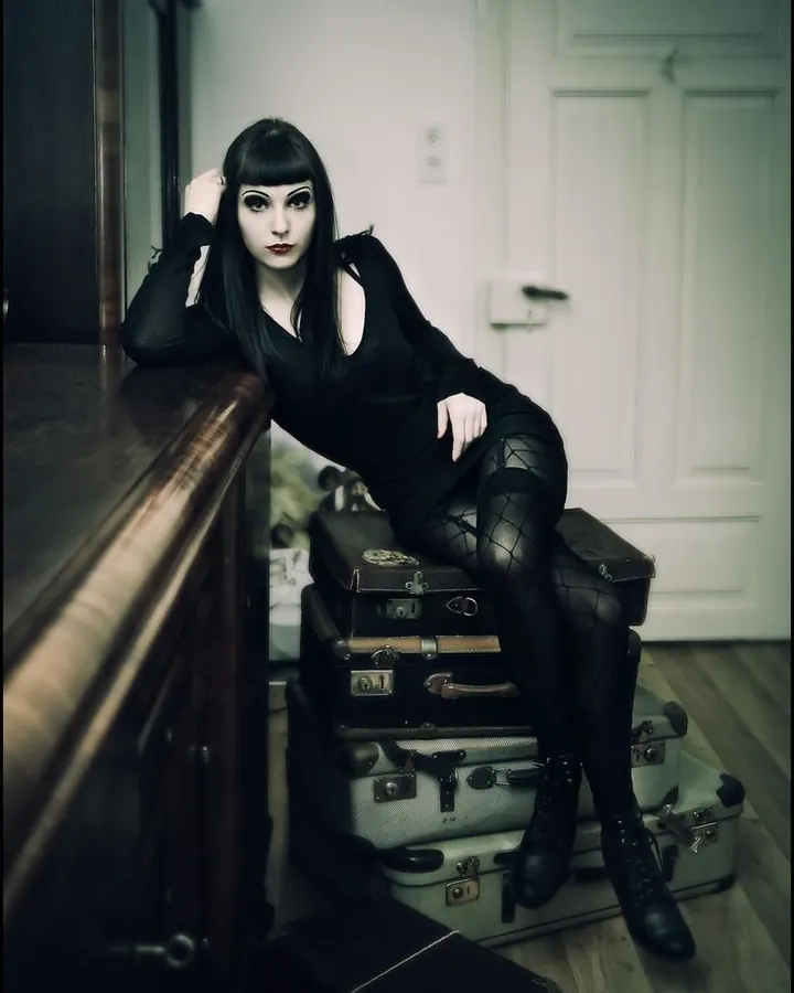 Femme trans en lingerie noire, cheveux bruns, pose sensuelle sur un lit, regard vers l'objectif.