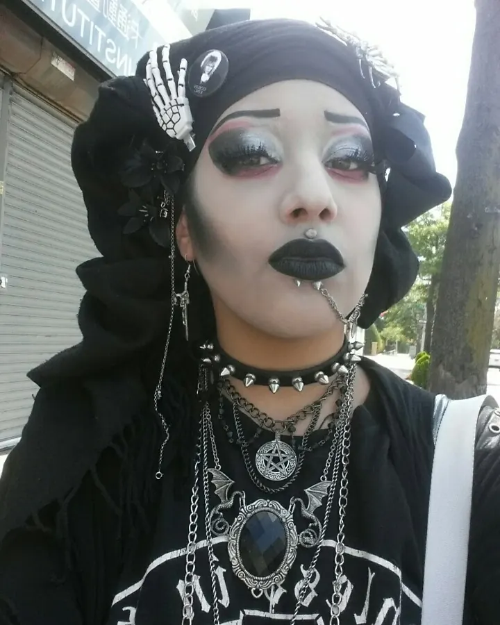 Femme trans aux cheveux noirs portant un haut blanc, assise dans une cuisine en tenant une tasse.