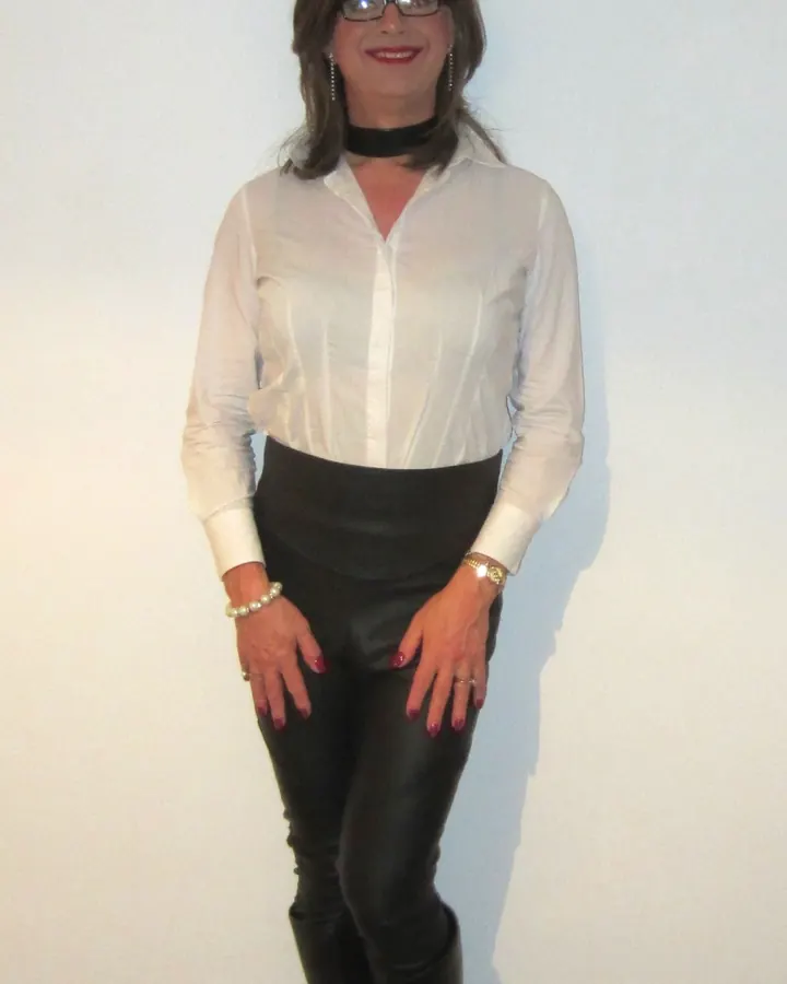 Femme trans aux cheveux blonds, en lingerie noire, posant sur une terrasse tropicale.